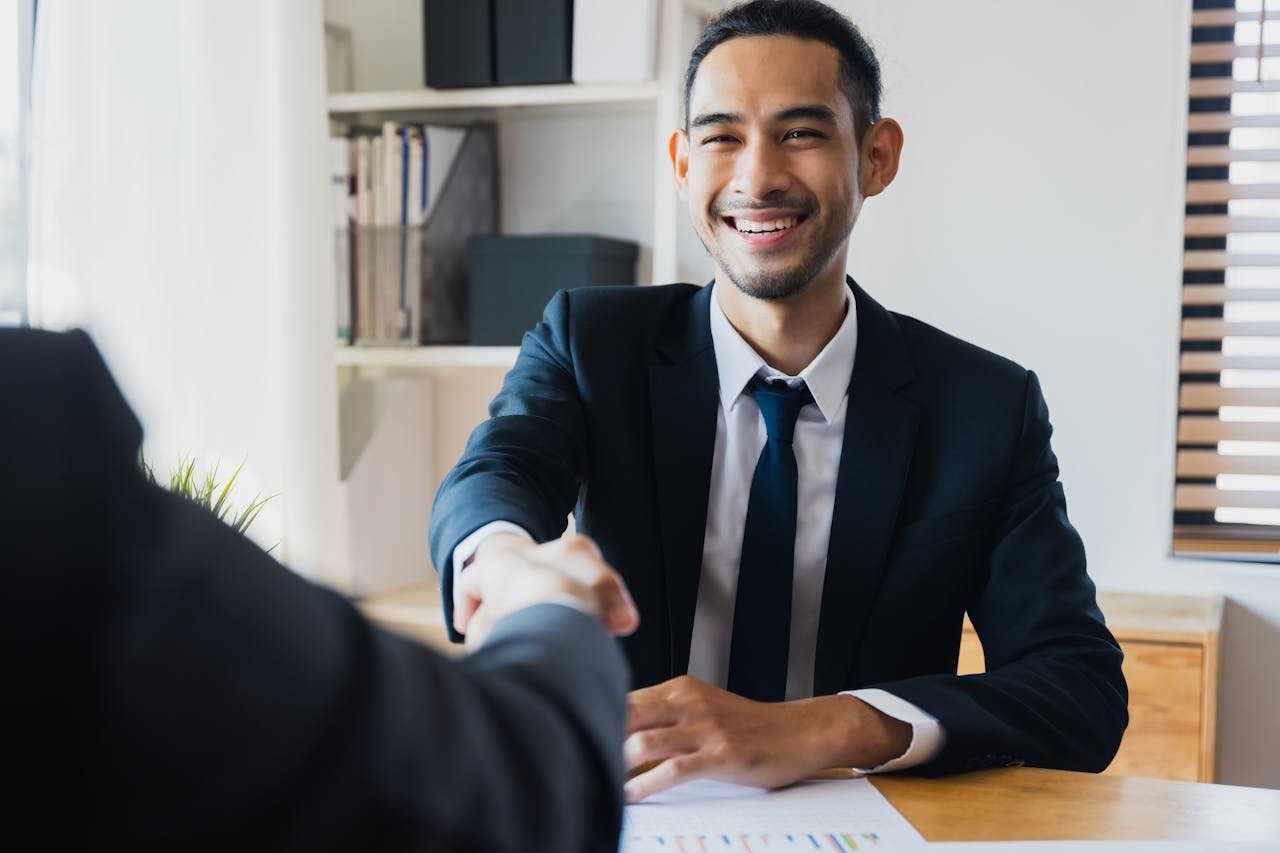 Contact Confident businessman in suit shaking hands at office desk, symbolizing successful partnership.